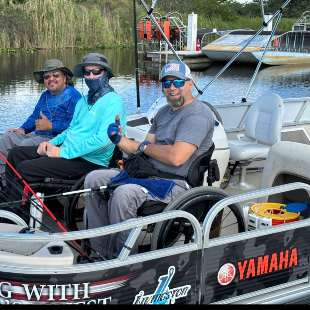Three men in wheelchairs on a Yamaha boat on a lake with a ferry in the background.