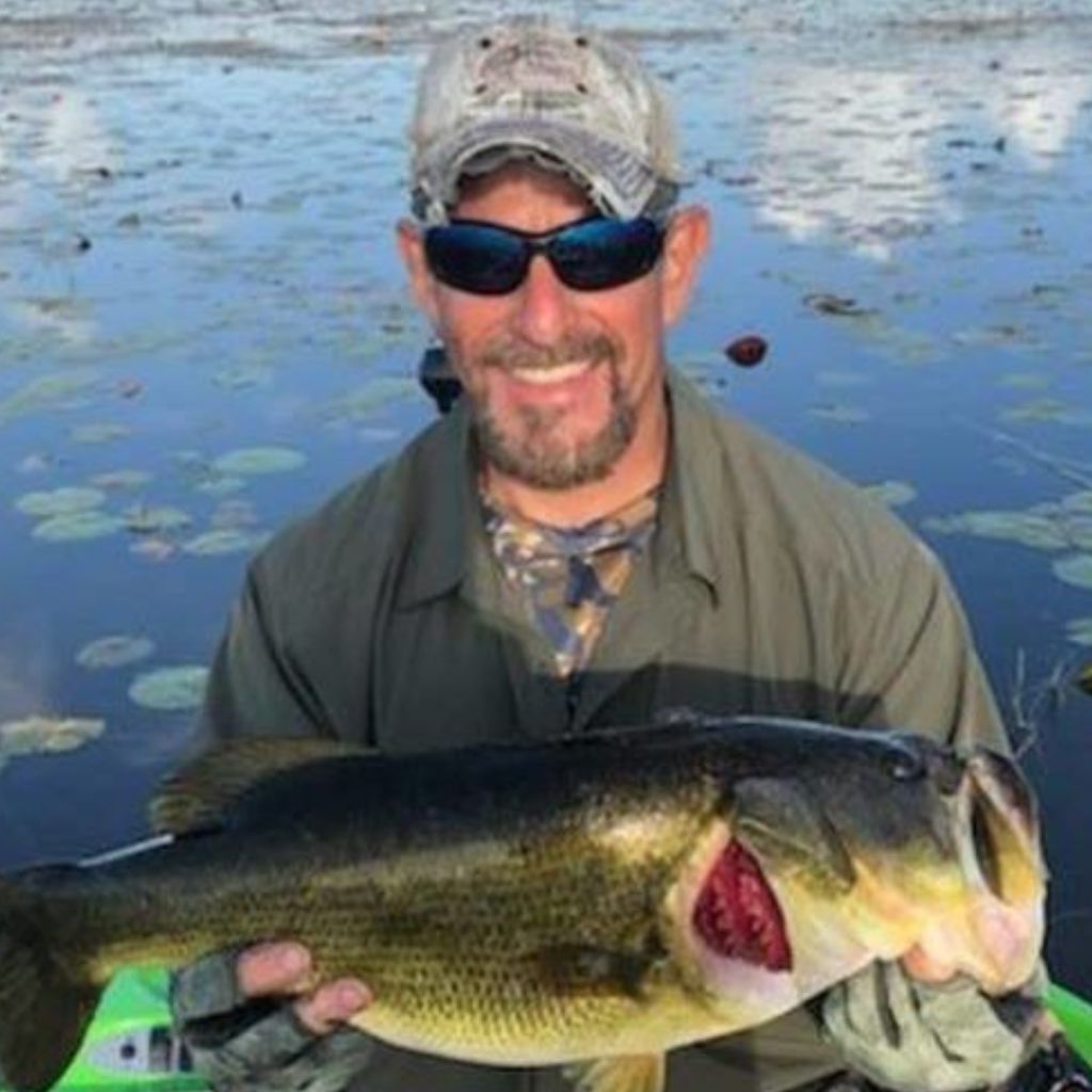 Man holding a large fish by a body of water