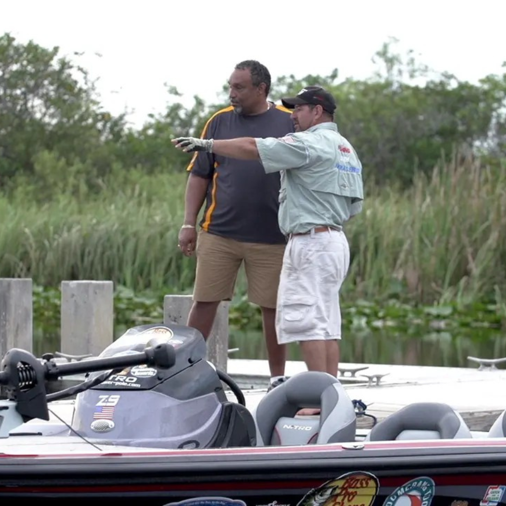 Two men standing next to a boat on a grassy area with trees in the background